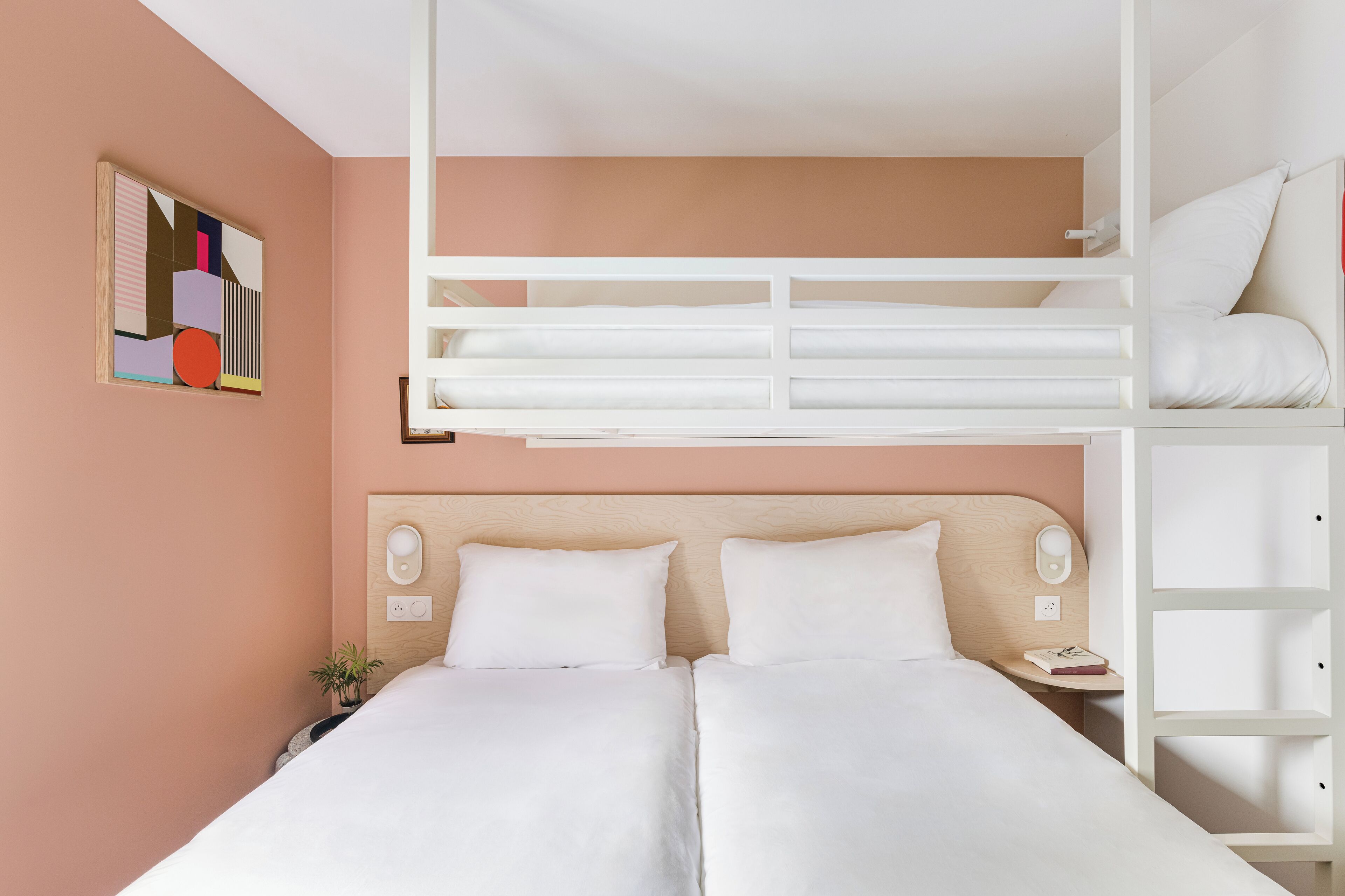 A hotel room with a bunk bed, a bedside table with a lamp, and a wall-mounted artwork.