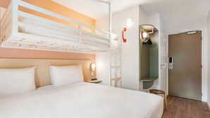 Una habitación de hotel con una cama litera, una mesita de noche con lámpara, un armario y una puerta.