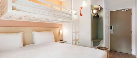 Una habitación de hotel con una cama litera, una mesita de noche con lámpara, un armario y una puerta.