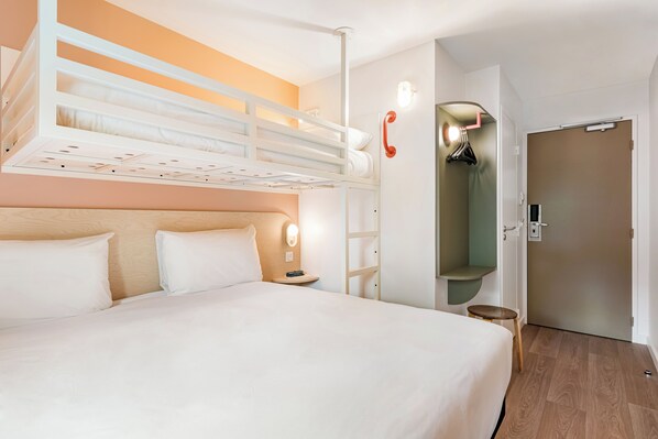 Una habitación de hotel con una cama litera, una mesita de noche con lámpara, un armario y una puerta.