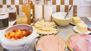 A kitchen counter with various food items and kitchenware, including a bowl of fruit, cheese, butter, and milk bottles.