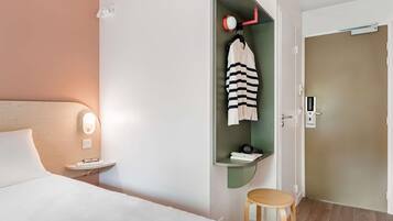 Een hotelkamer met een bed, nachtkastje, wandlamp, plank met een handdoek en een deur met slot.