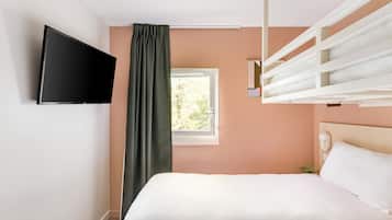 Un dormitorio con cama, televisor montado en la pared, ventana con cortinas y cabecera con lámpara.