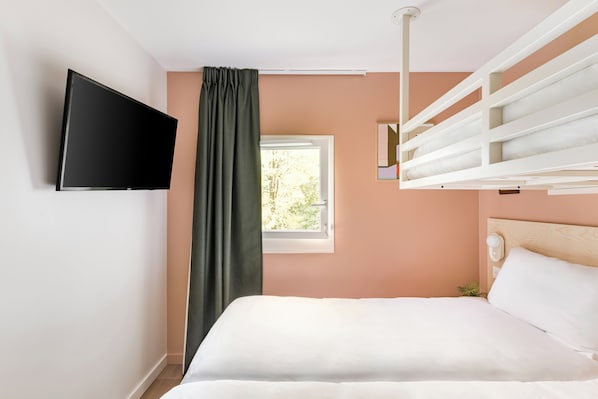 Un dormitorio con cama, televisor montado en la pared, ventana con cortinas y cabecera con lámpara.