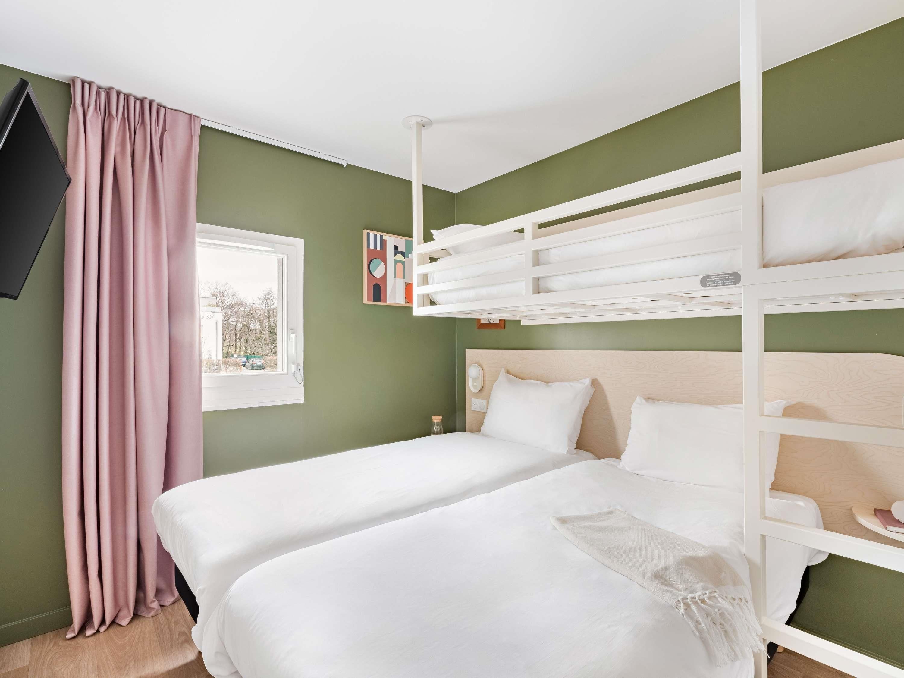 Una habitación con literas, una ventana con cortinas, un televisor de pantalla plana y una mesita.