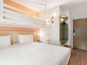 Habitación de hotel con literas, una mesita de noche, una lámpara, un armario y zona de ducha.