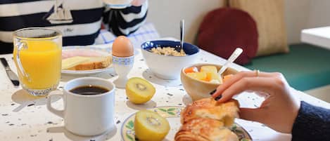 A breakfast table with a glass of orange juice, a cup of coffee, a plate with toast, a kiwi, a croissant, and a bowl of cereal.