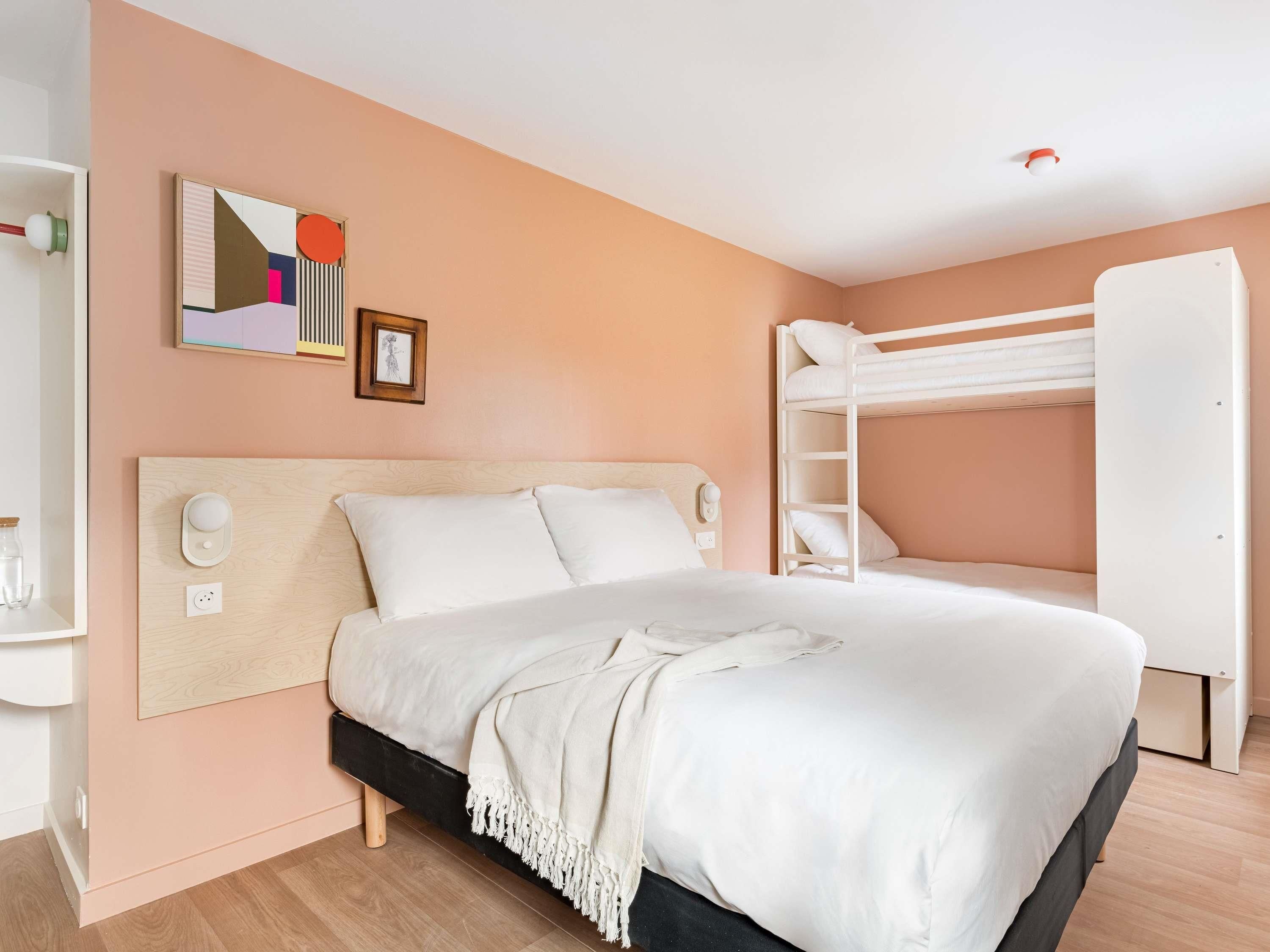 Een slaapkamer met een stapelbed, een nachtkastje, een wandlamp en een lijst met een afbeelding.