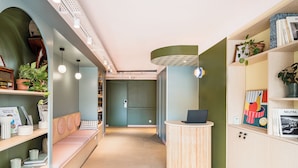 Una recepción moderna con un mostrador de madera, una zona de estar con un banco y estanterías con libros y objetos decorativos.