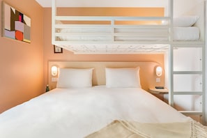 Una cama bien hecha con cabecera, una mesita de noche con lámpara y una cama nido encima.
