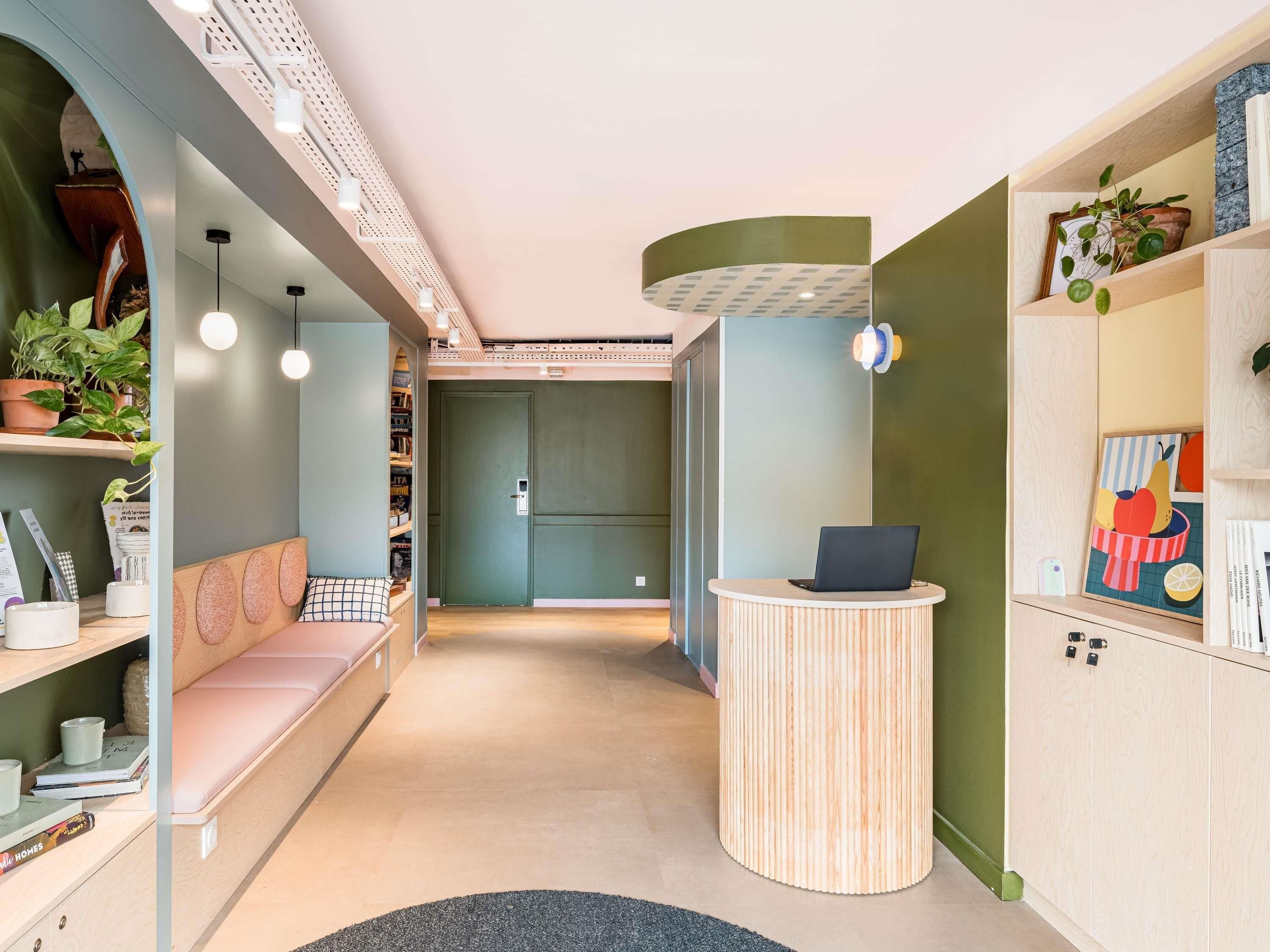 A modern interior with a curved reception desk, a seating area with a bench, and shelves with plants and books.