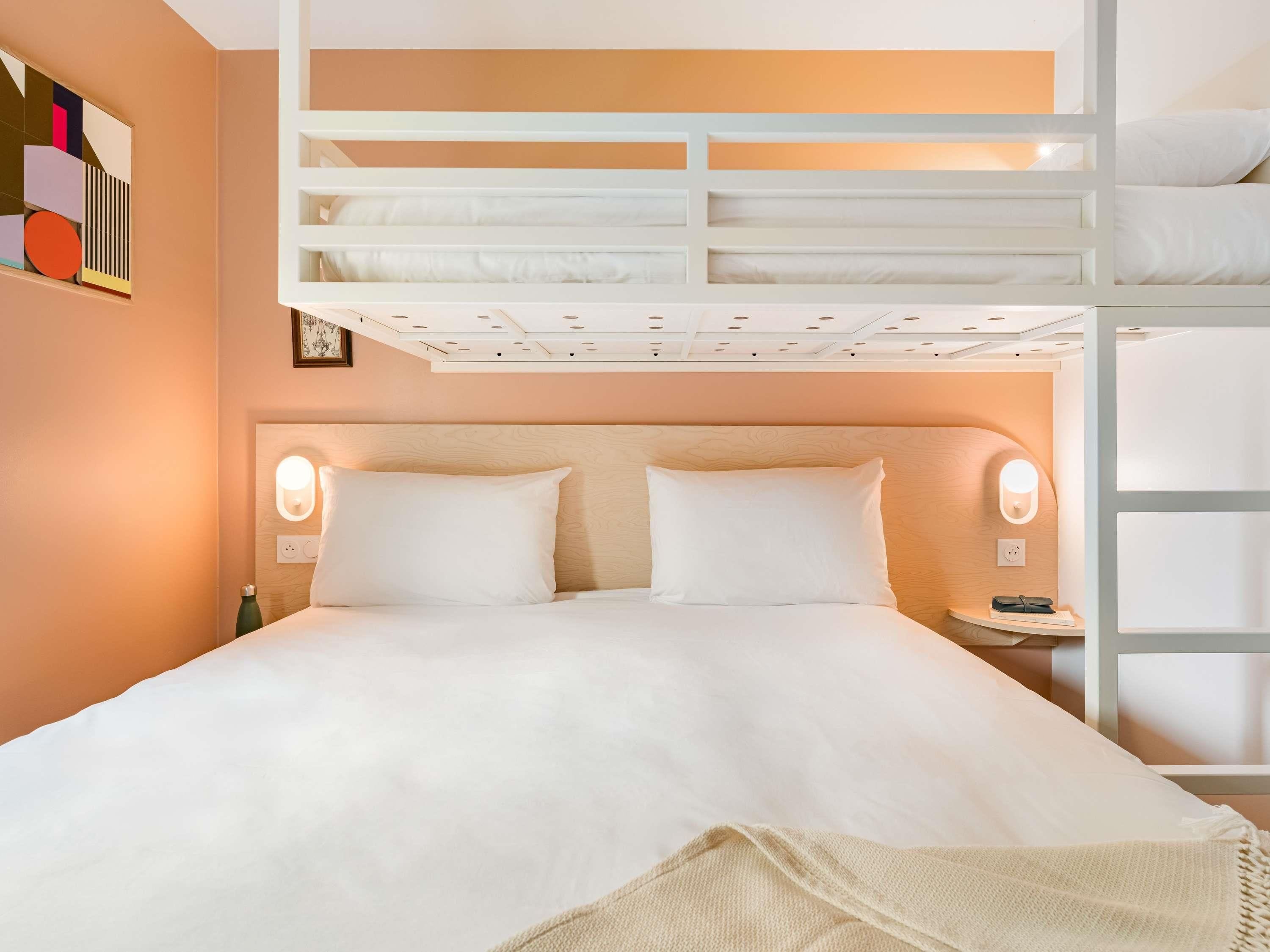 Habitación de hotel con una cama litera, una mesita de noche y un aplique de pared.