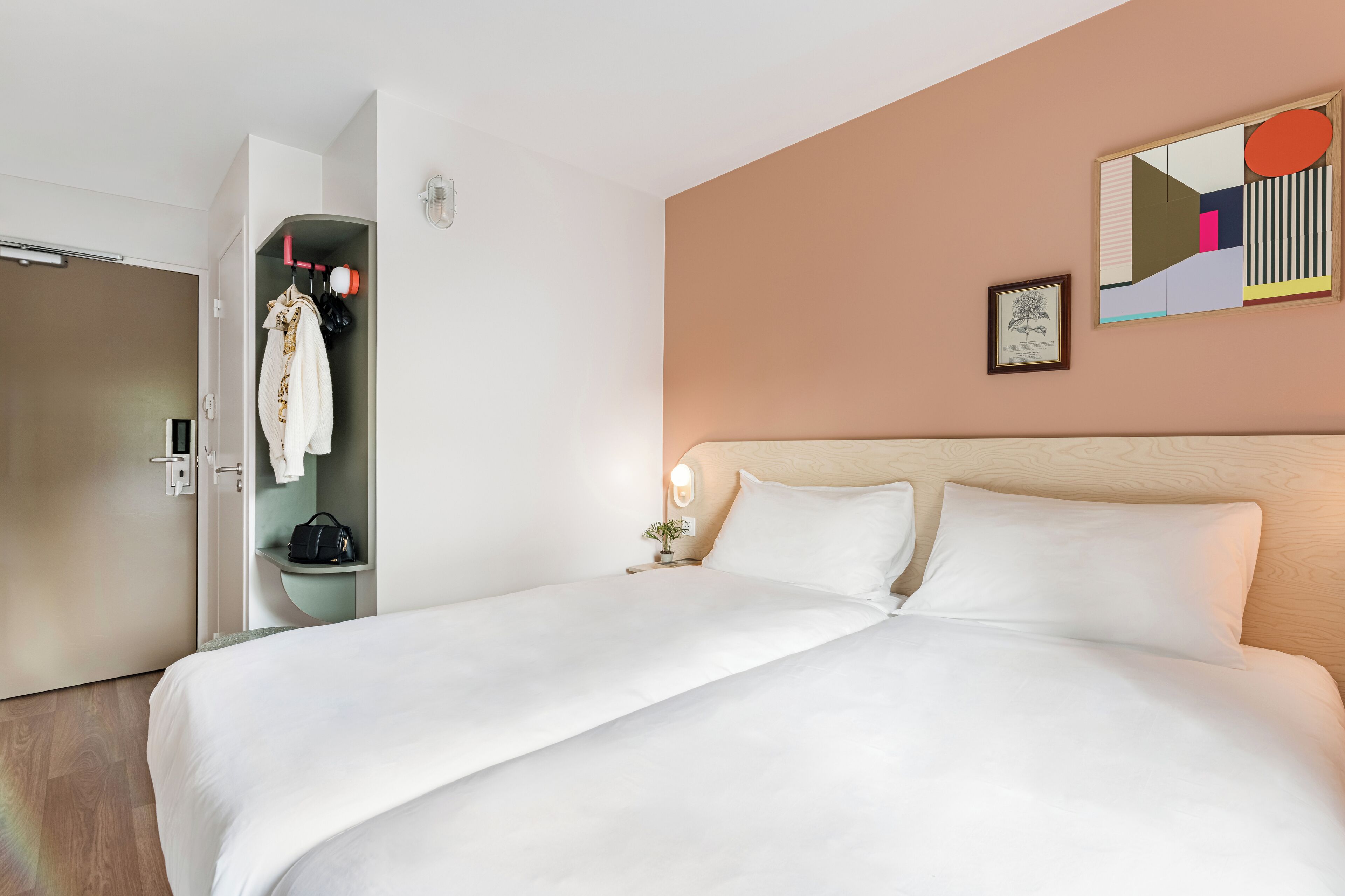 A hotel room with a large bed, a wardrobe, a nightstand with a lamp, and a framed picture on the wall.