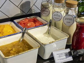 Ein Buffet mit verschiedenen Speisen, darunter Obst, ein Joghurtgetränk und ein Glas Rotsoße.
