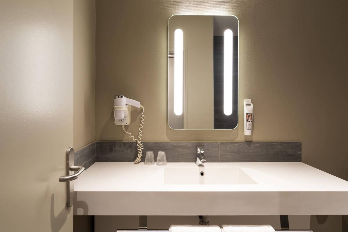 Un baño con un espejo grande, un lavabo, un secador de pelo y una botella de loción.