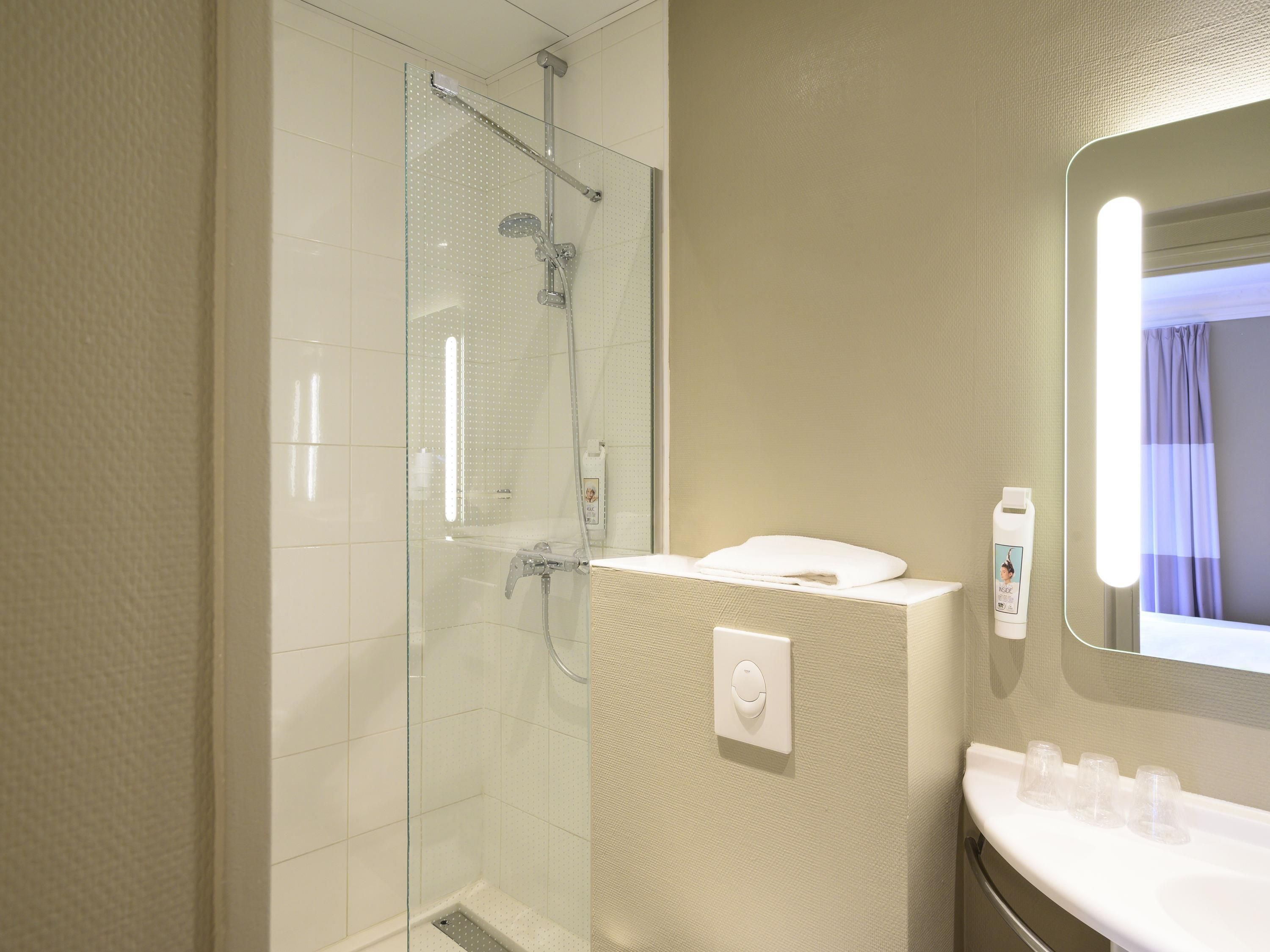 Une salle de bain moderne avec une douche à parois de verre, un lavabo blanc avec un miroir et une serviette posée sur le comptoir.
