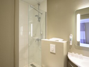 Un baño moderno con cabina de ducha de vidrio, un lavabo blanco con espejo y una toalla sobre el mostrador.