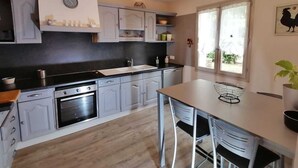 A modern kitchen with grey cabinets, a black countertop, and a built-in oven. There is a window with a view of greenery outside. - Josephine's House with swimming pool (Pierrelatte)