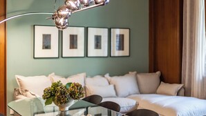Ett modernt vardagsrum med ett soffbord i glas, en soffa och en matplats med stolar. Det finns inramade tavlor på väggen och en prydnadsväxt på bordet.