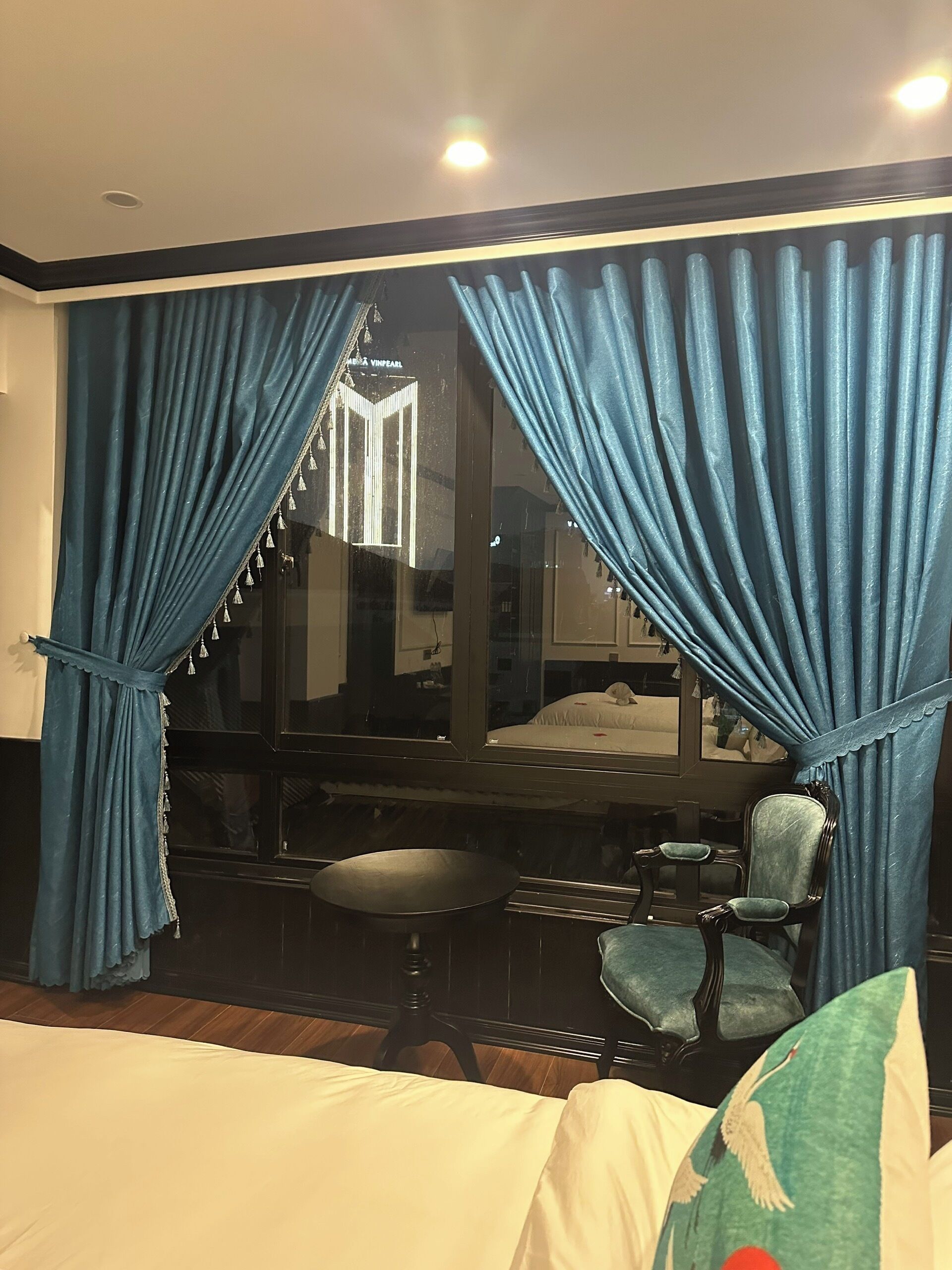 A hotel room with a bed, a chair, a small table, and a large window with blue curtains.