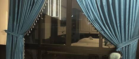 A hotel room with a bed, a chair, a small table, and a large window with blue curtains.