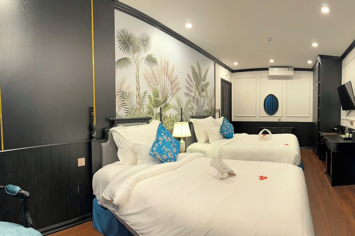 A hotel room with two beds, a TV, a desk, and a wall with a tropical mural.