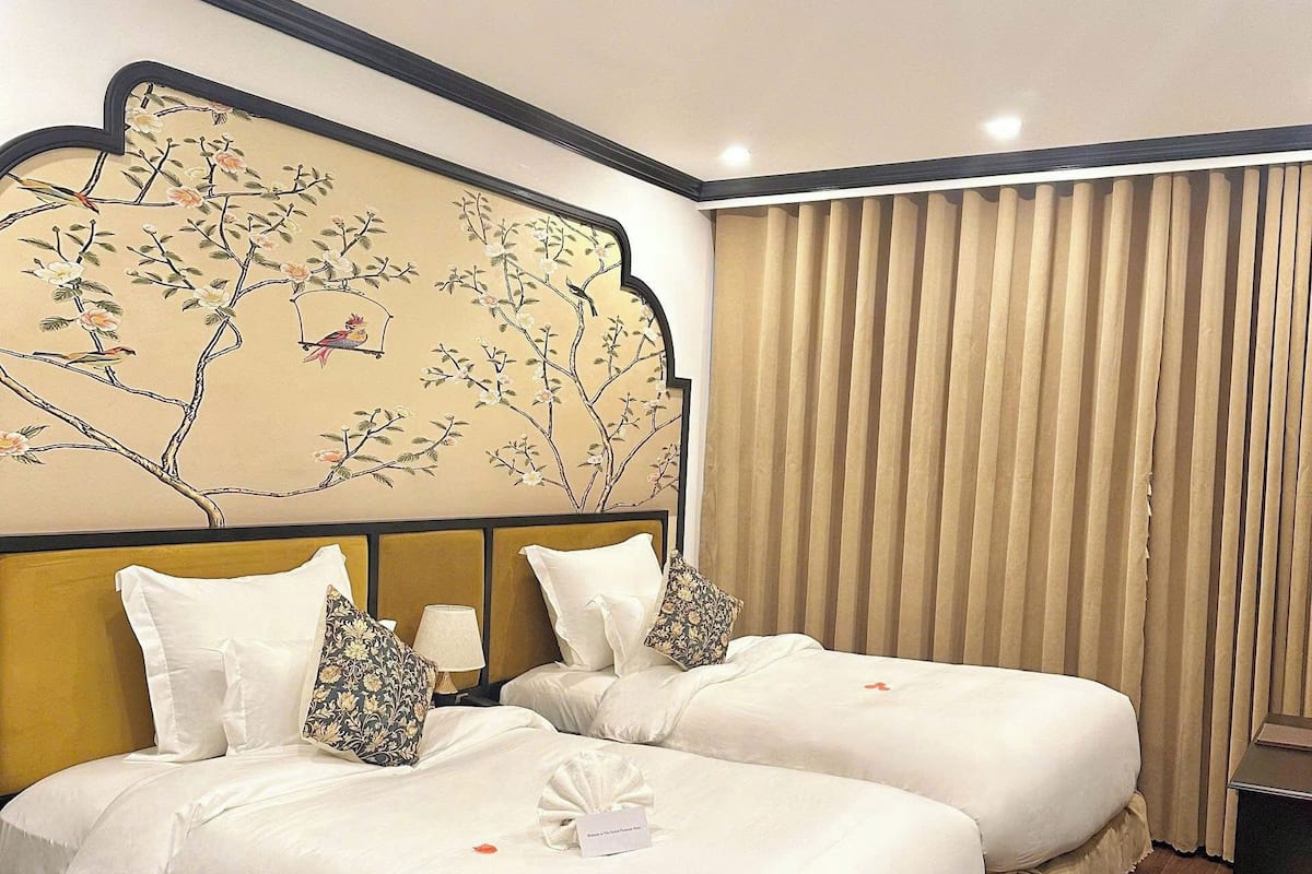 A hotel room with two beds, a decorative wall panel, and a curtain.