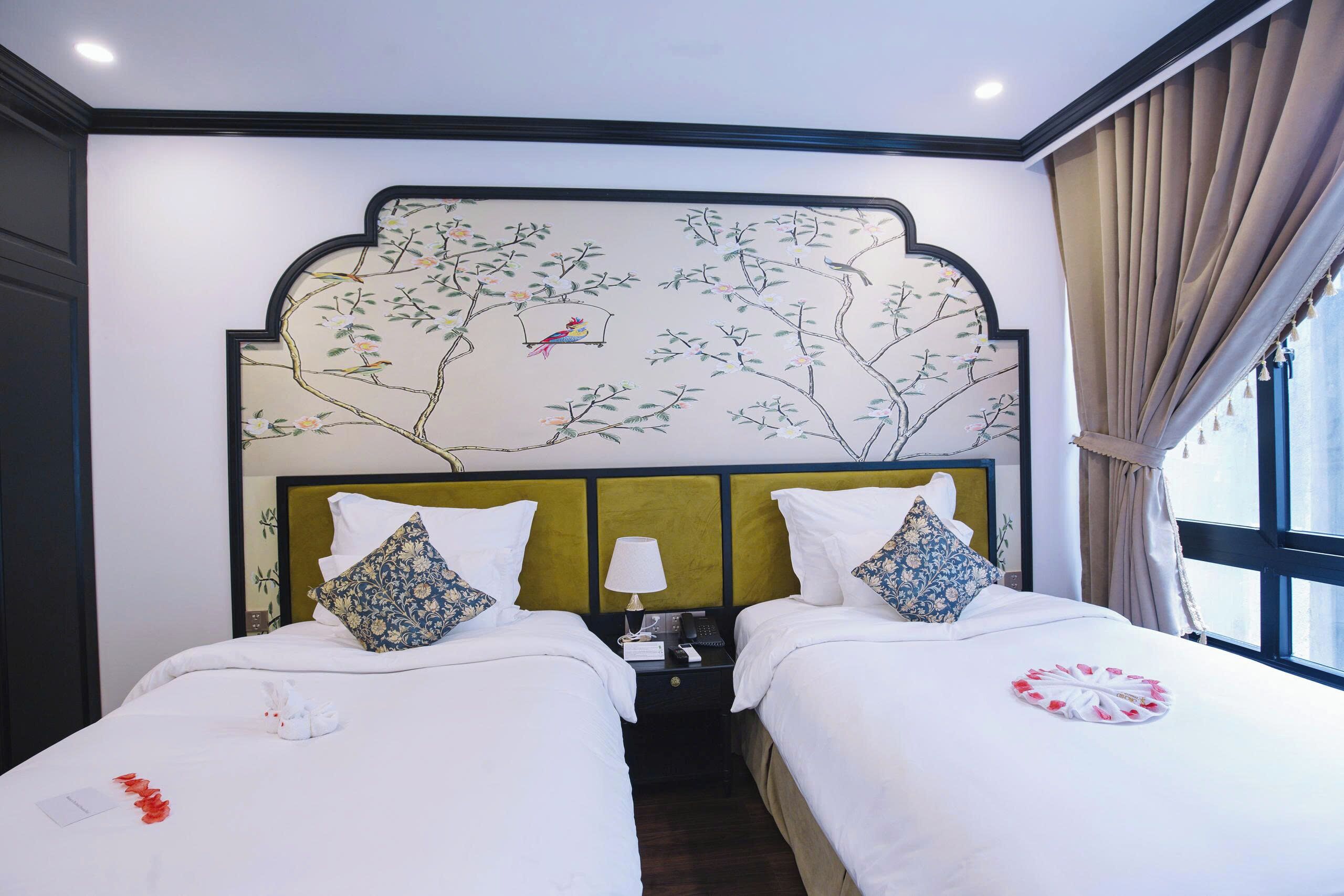 A hotel room with two beds, a green headboard, and a wall mural of a tree with birds.