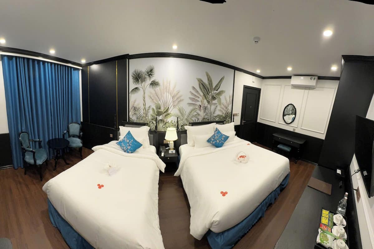 A hotel room with two beds, a desk, a chair, a TV, and a wall with a tropical mural.