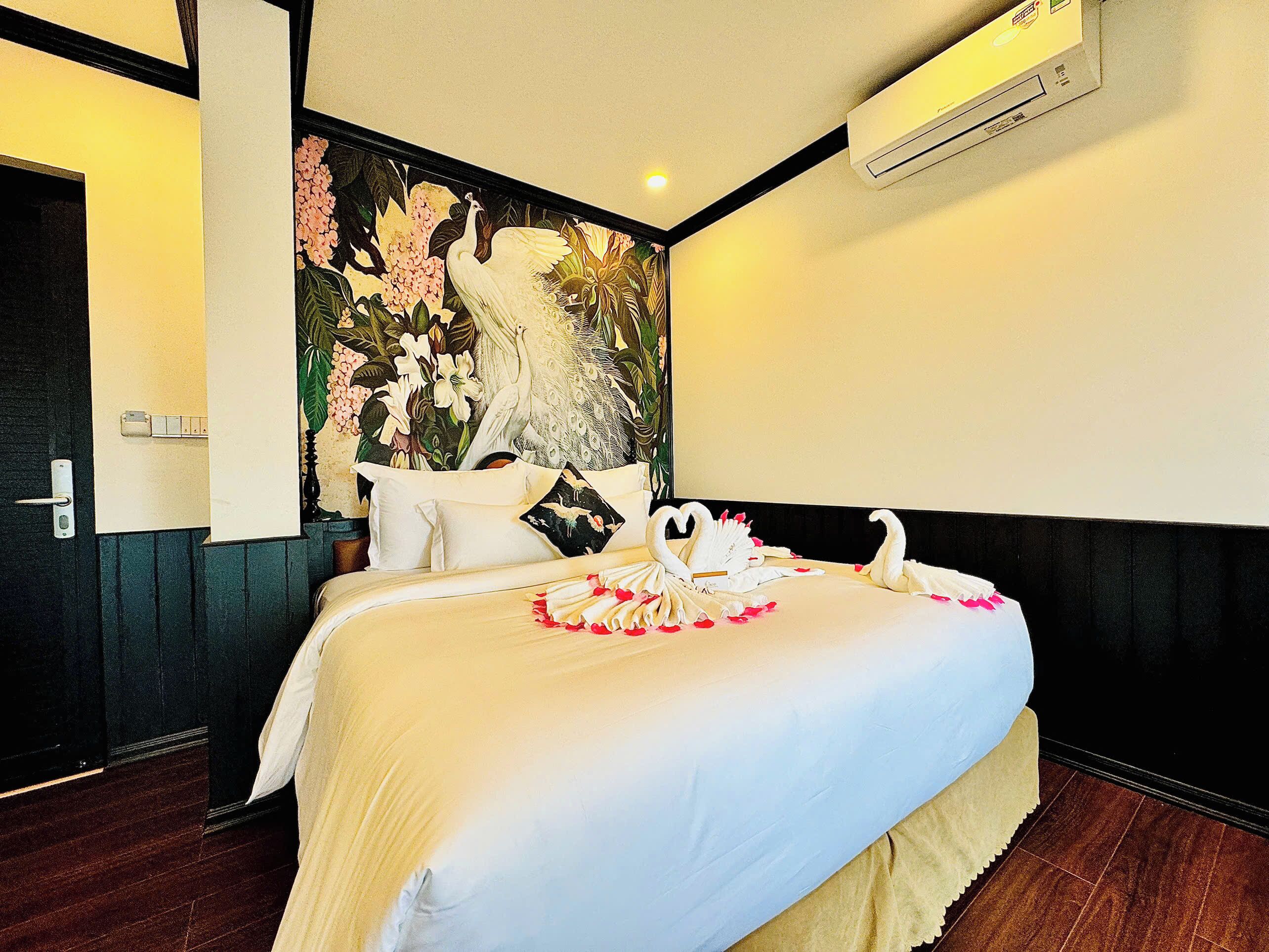 A hotel room with a large bed, a floral headboard, and an air conditioning unit above the bed.