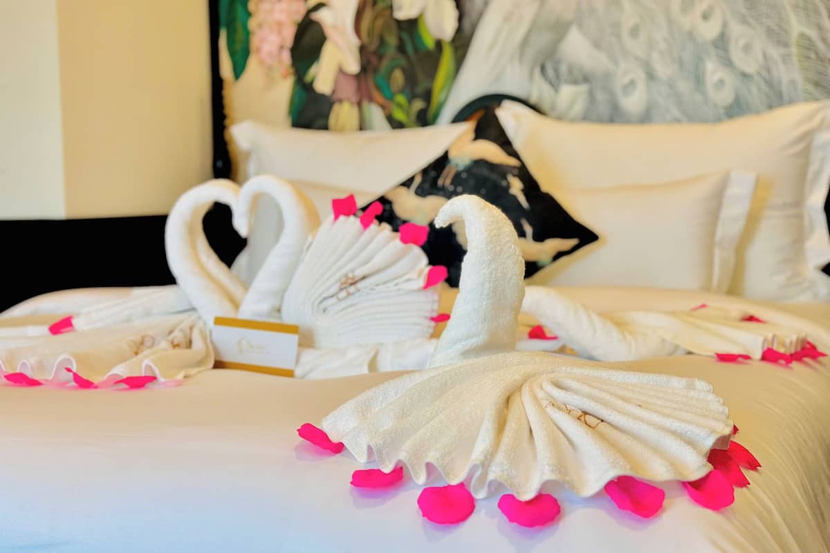 A neatly made bed with two swan-shaped towels and pink rose petals.