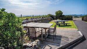Patio esterno con tavolo e sedie di legno, tavolo da picnic e vista sul mare.