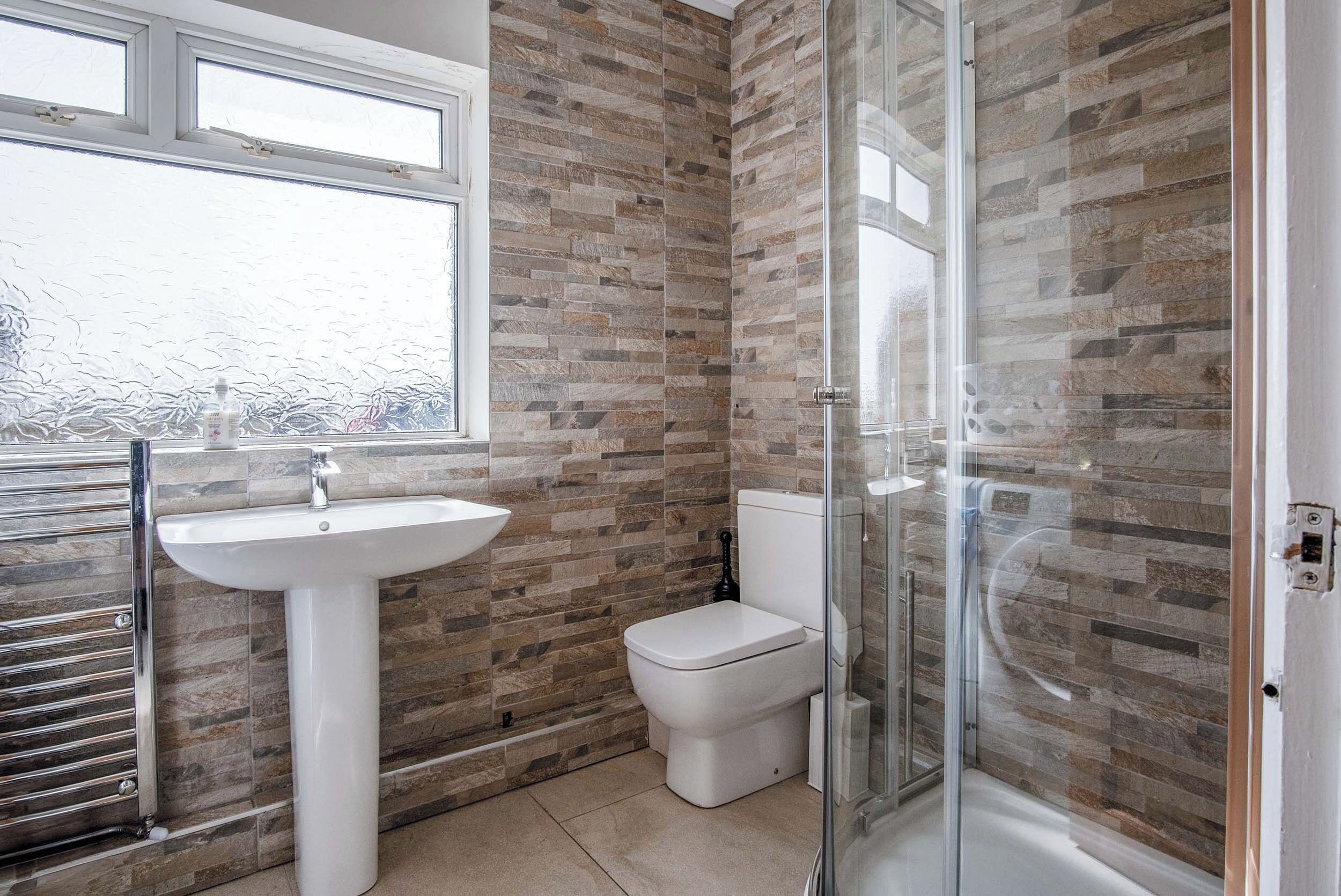 A bathroom with a stone-patterned wall, a white sink, a toilet, and a glass-enclosed shower.