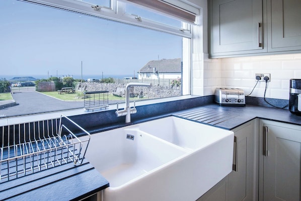 A kitchen with a large window, a sink, and a dish rack. - Channel View 3 Bedroom Rhossili Bay (Swansea)