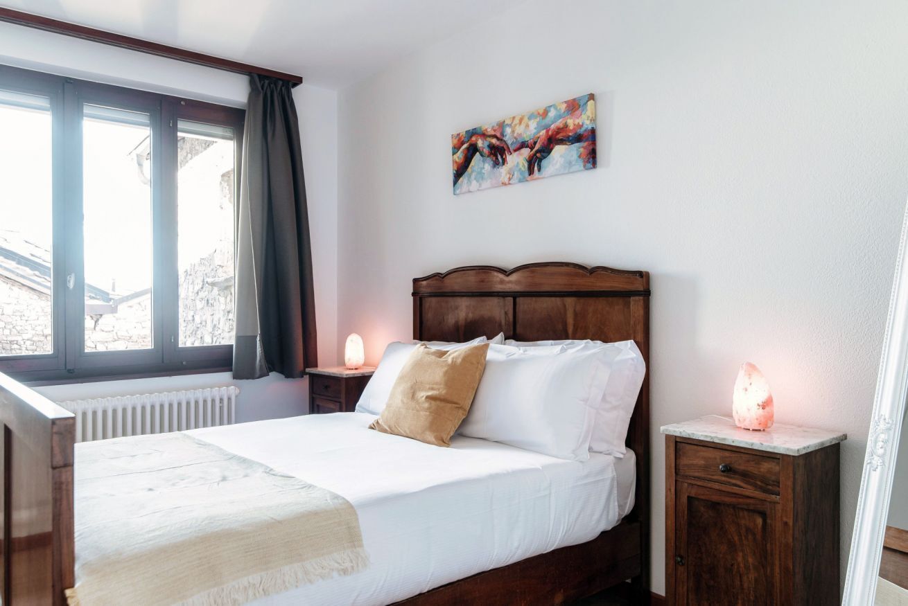Ein ordentlich bezogenes Bett mit weißen Leinentüchern und einer braunen Decke, ein hölzernes Kopfende, ein Nachttisch mit einer Lampe und ein Bild an der Wand.