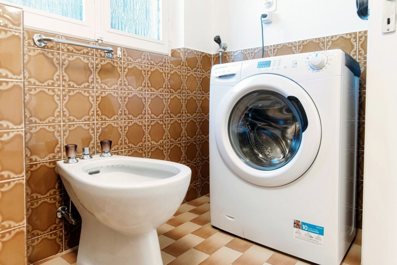 Ein Badezimmer mit Waschmaschine, Bidet und gemusterten Fliesen.