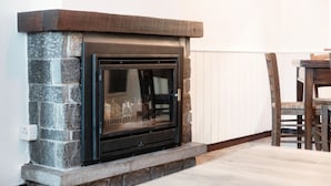 A stone fireplace with a black glass door, located in a room with a wooden table and chairs. - Historic house in the artistic village of Brè (THE SECRET GARDEN) (Lugano)