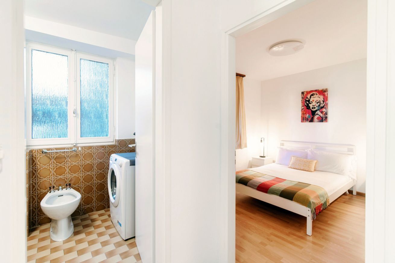 Ein Zimmer mit einem Bett, einem Fenster, einer Waschmaschine und einem Bidet.