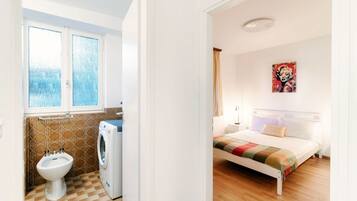 Ein Zimmer mit einem Bett, einem Fenster, einer Waschmaschine und einem Bidet.