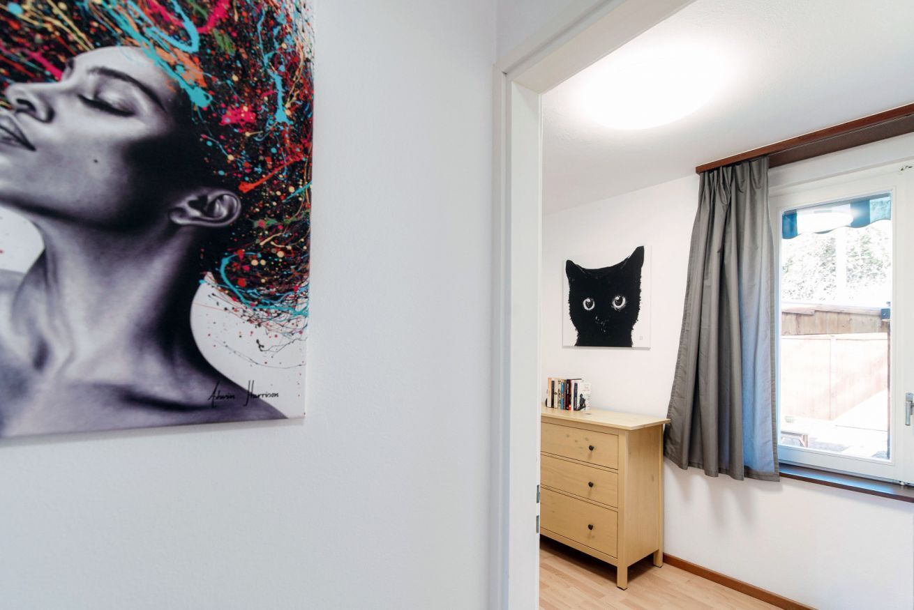 Una habitación con un aparador de madera, una ventana con cortinas y una pared con un gato negro y un cuadro abstracto colorido.
