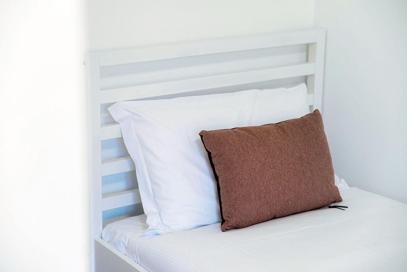A white bed with a brown pillow and white bedding.