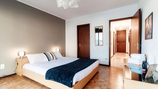 A bedroom with a bed, bedside lamps, a wooden door, and a small desk with a telephone.