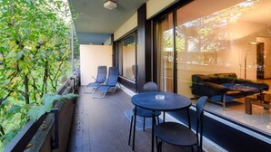 A balcony with a table and chairs, a sofa, and a large window with a view of greenery.