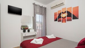 A hotel room with a bed, a TV, a desk with a mirror, a window with curtains, and wall art.