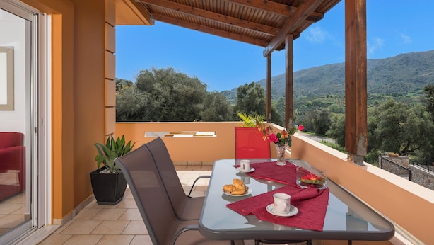 A balcony with a table set for two, a potted plant, and a view of the countryside.