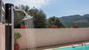 A pool with a water feature, potted plants, and a view of hills.