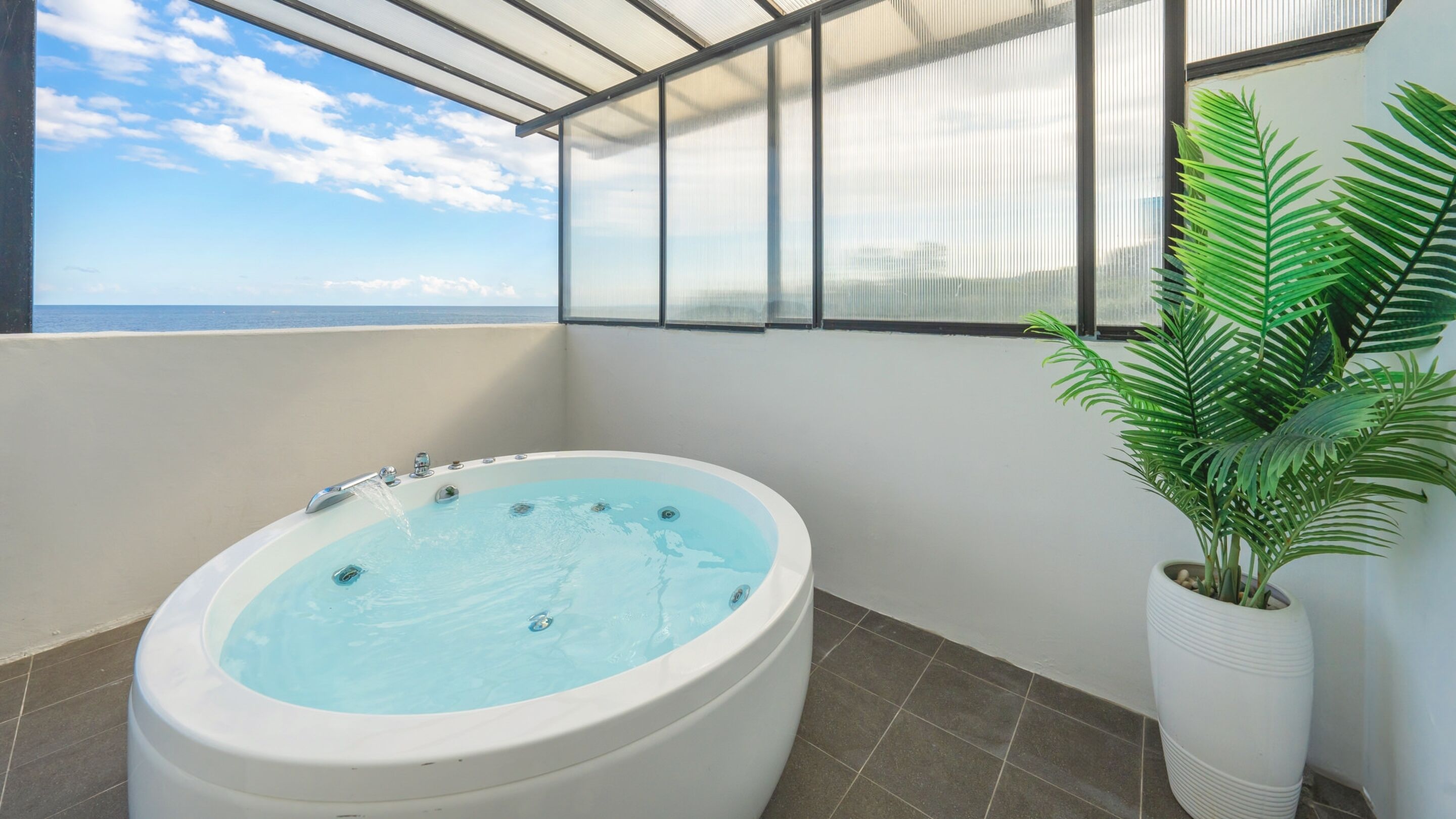 A bathroom with a large bathtub, a potted plant, and a view of the ocean.