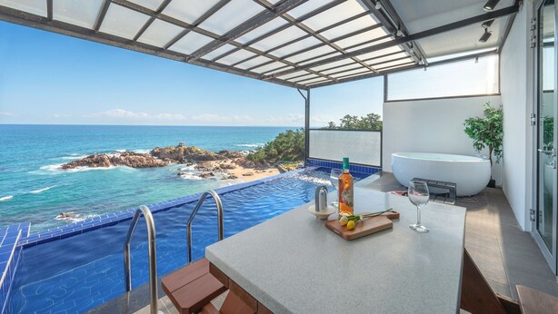 Een balkon met uitzicht op de oceaan, een bubbelbad en een tafel met een fles en een glas.
