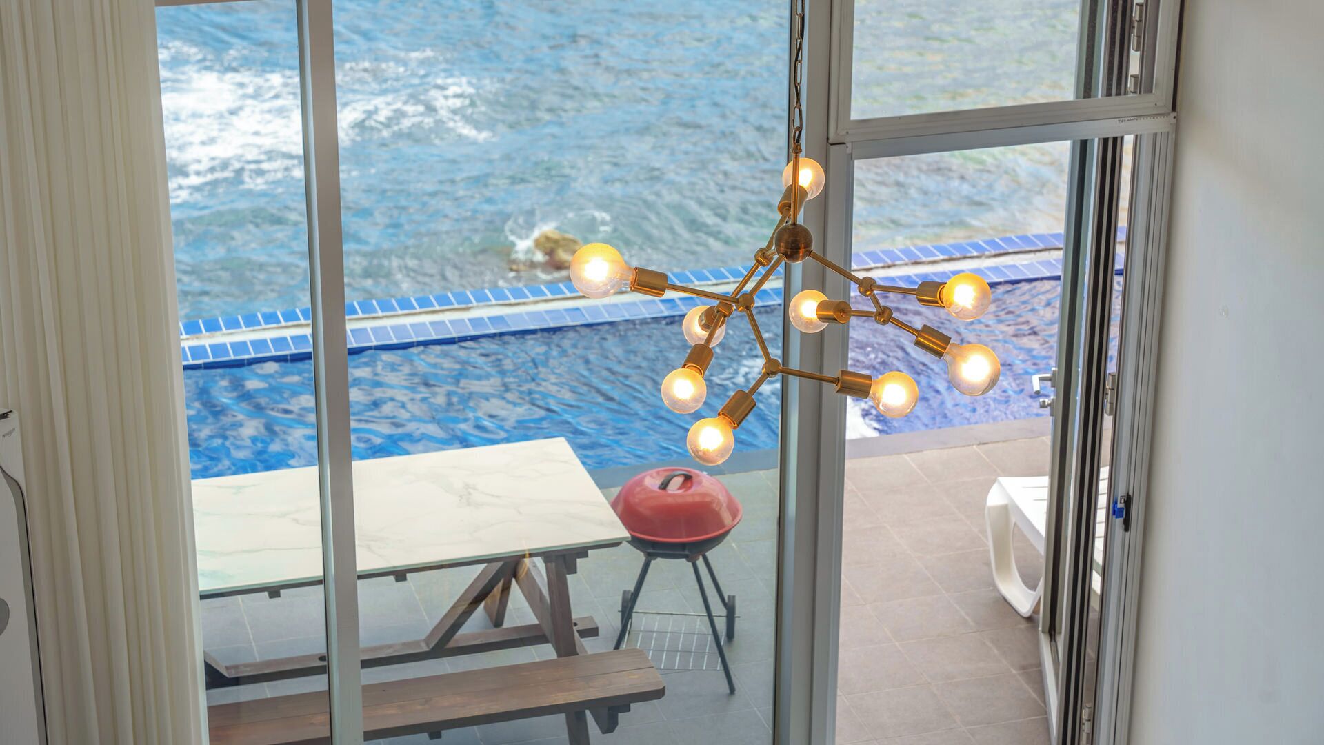 A poolside area with a hanging light fixture, a picnic table, and a red chair.