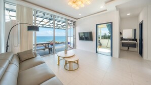 Een moderne woonkamer met een groot raam met uitzicht op zee, een bank, een ronde tafel en een aan de muur bevestigde televisie.